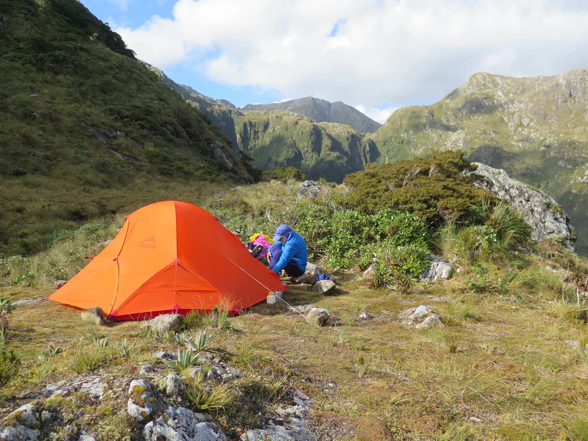Hikers Camping on Henry Pass with Bright Orange Tent, Fiordland Outdoors