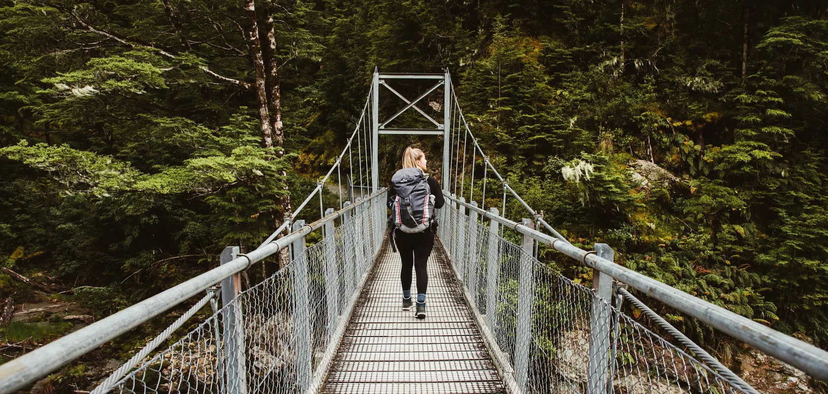 Hiker walking across swing bridge in the National Park, Routeburn Track, Fiordland Outdoors