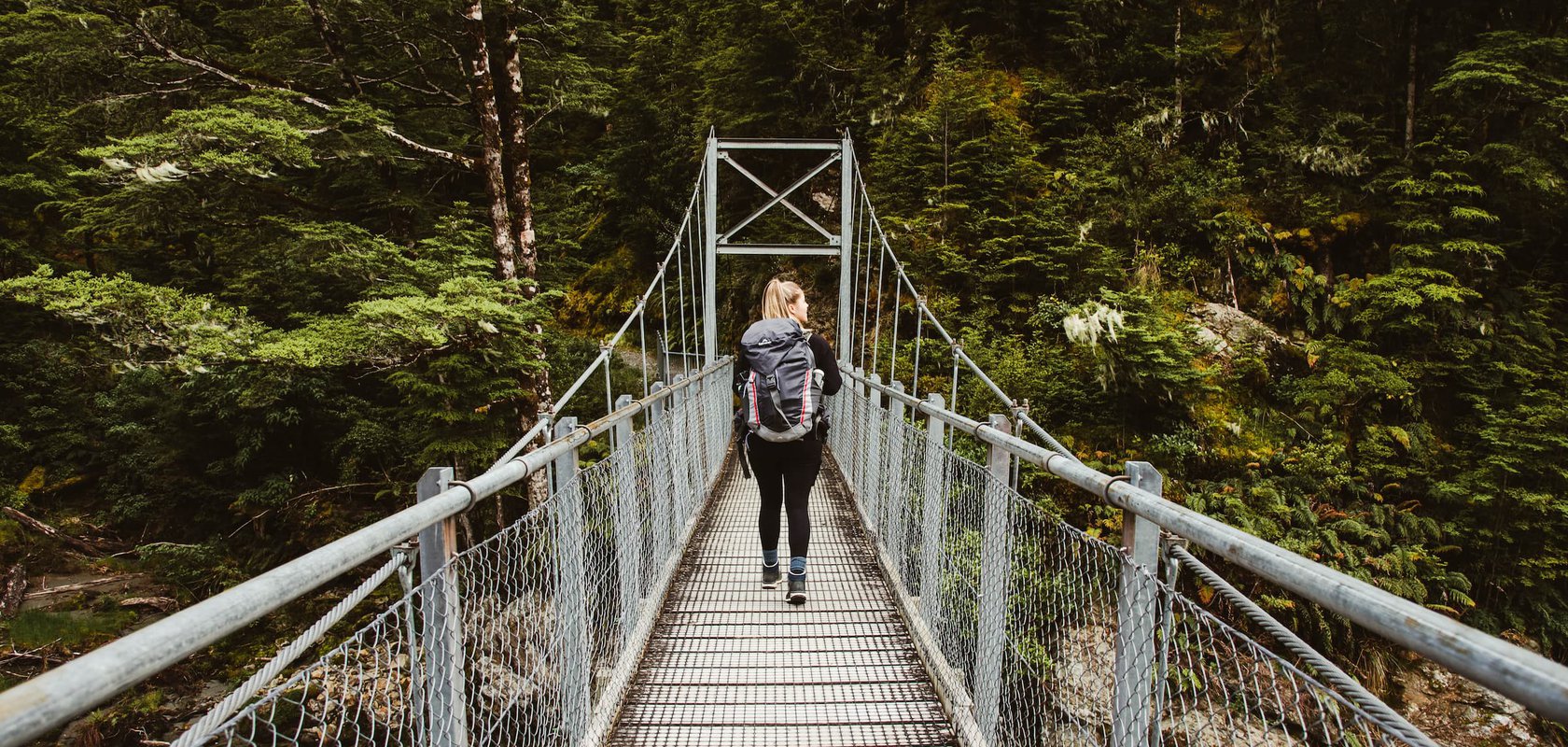 Hiker walking across swing bridge in the National Park, Routeburn Track, Fiordland Outdoors Co